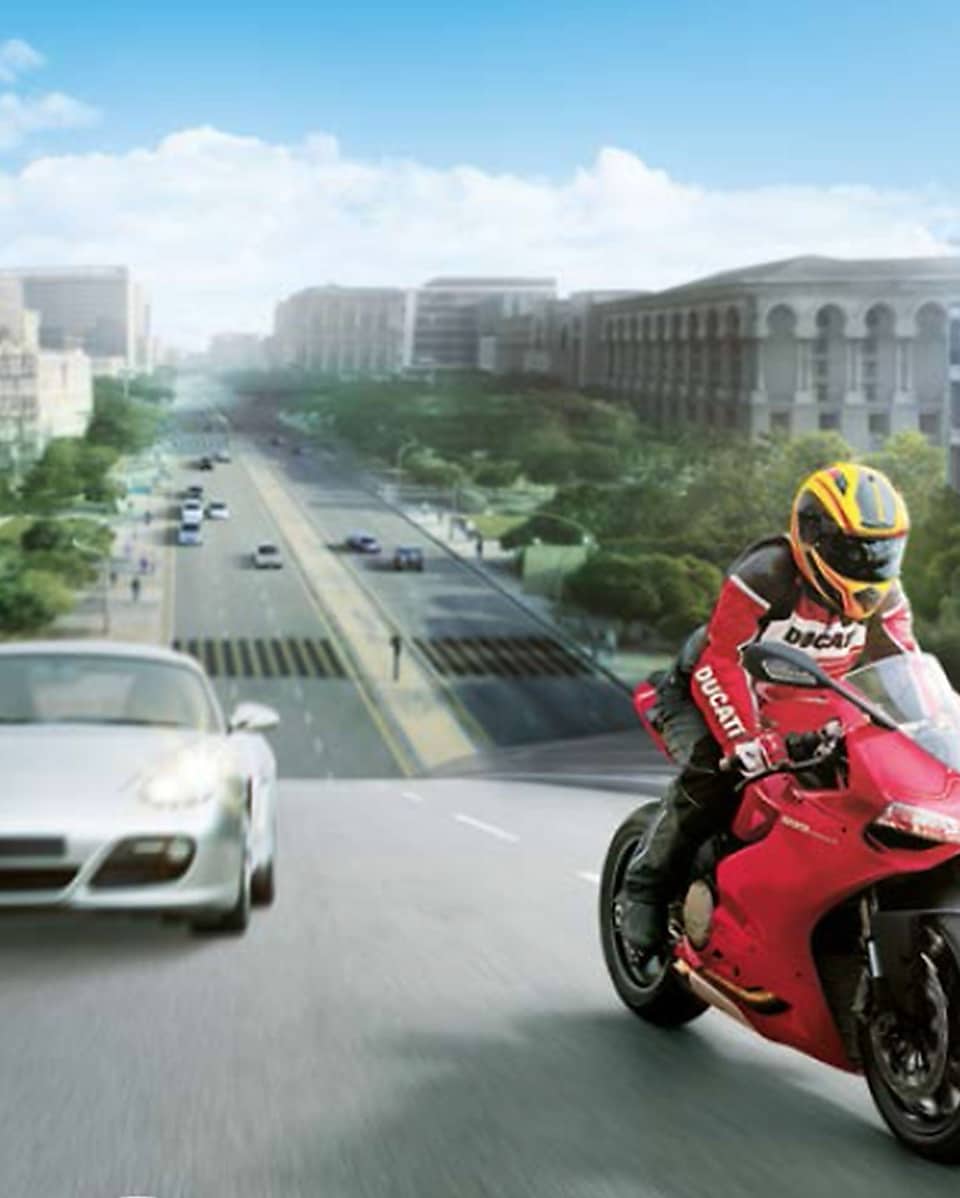 Moto rouge et conducteur sur une route avec des voitures et des bâtiments dans l&rsquo;arrière-plan.