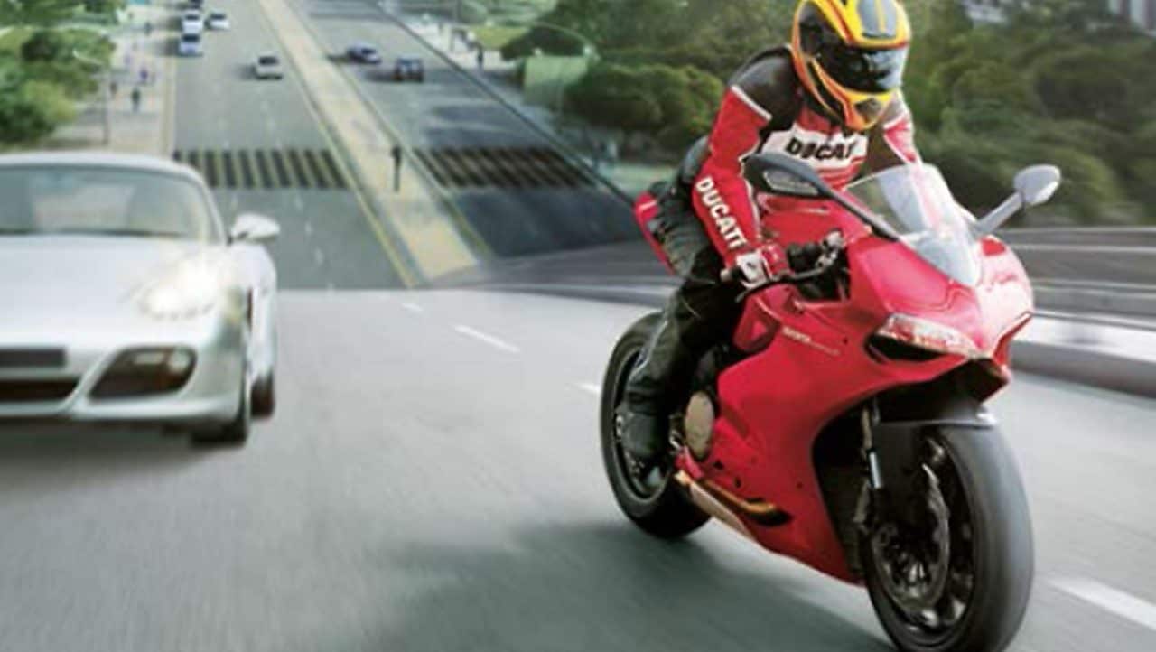 Moto rouge et conducteur sur une route avec des voitures et des bâtiments dans l’arrière-plan.